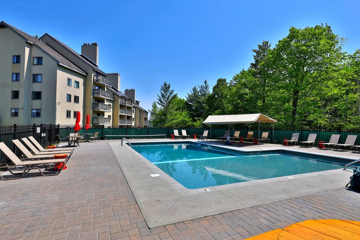 This exterior image showcases a swimming pool surrounded by lounge chairs, a canopy, and lush greenery. The setting is bright and open, creating a sense of relaxation and connection to the outdoors. The pool area is inviting, and the natural backdrop hints at the surrounding mountain environment, ideal for guests looking to enjoy Vermont's fresh air with their pets.