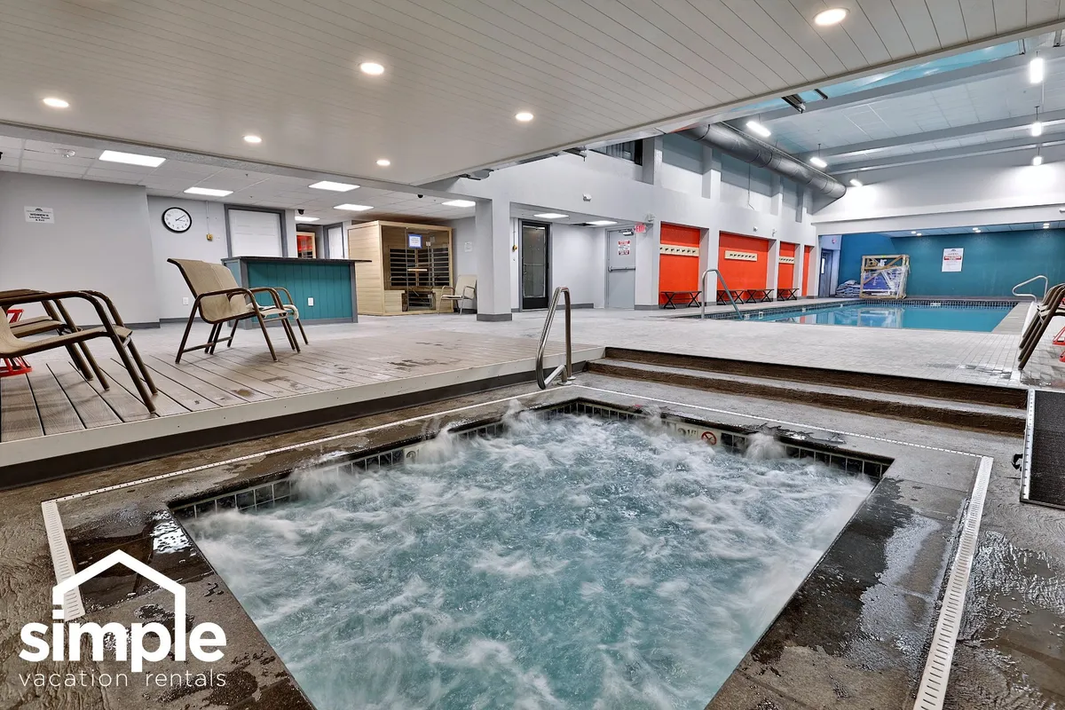 A tranquil wellness area featuring a hot tub adjacent to the swimming pool, with plenty of lounge chairs and a sauna area visible. The setting is peaceful and designed for relaxation after an active day.