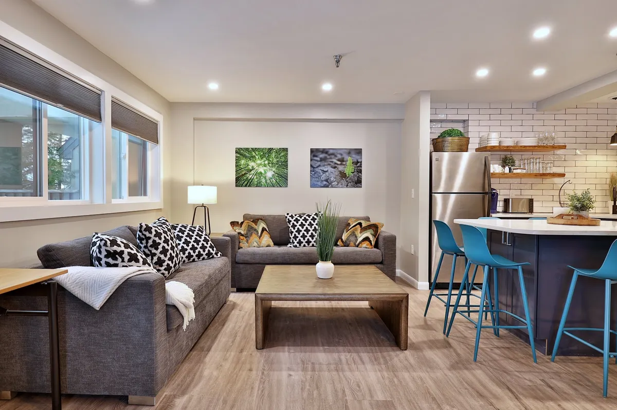 This shot showcases a comfortable living space with sofas, a coffee table, a kitchen island, and artistic touches. The open-concept design is evident, with the kitchen and living areas blending together, encouraging social interaction and group gatherings.