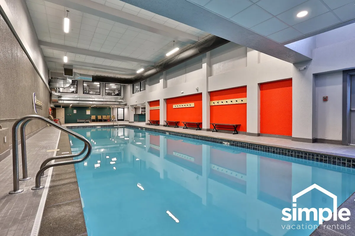 A vibrant indoor swimming pool with striking red accent walls. Benches line the poolside, inviting guests to relax or socialize. The area is brightly lit and has an energetic, welcoming atmosphere suitable for all seasons.