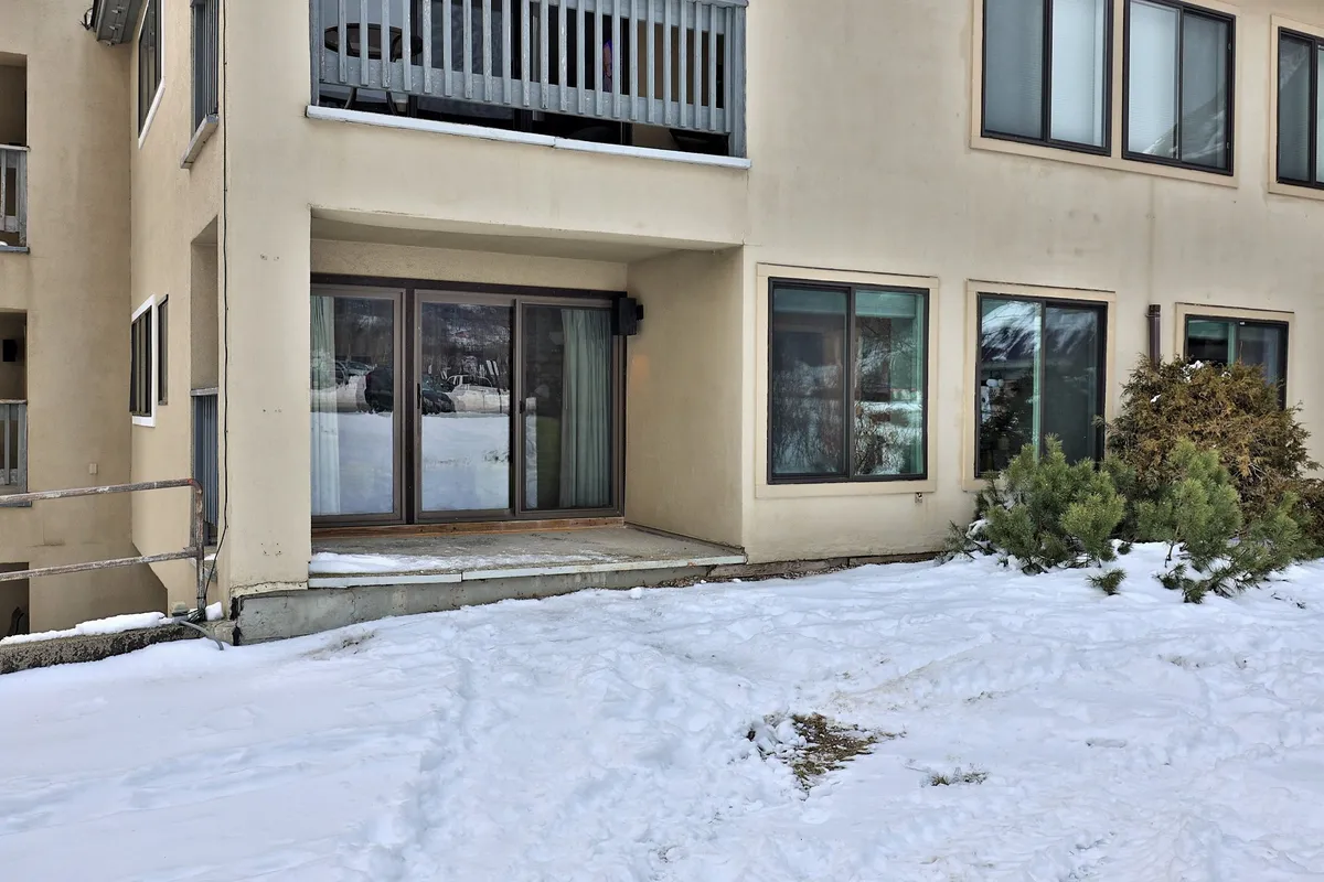 A serene exterior winter scene viewed from the property, featuring a snow-covered ground, sliding glass doors, and a balcony railing, all creating a cozy yet adventurous atmosphere. The scene hints at the proximity to outdoor activities and the ease of stepping out to explore local hotspots.