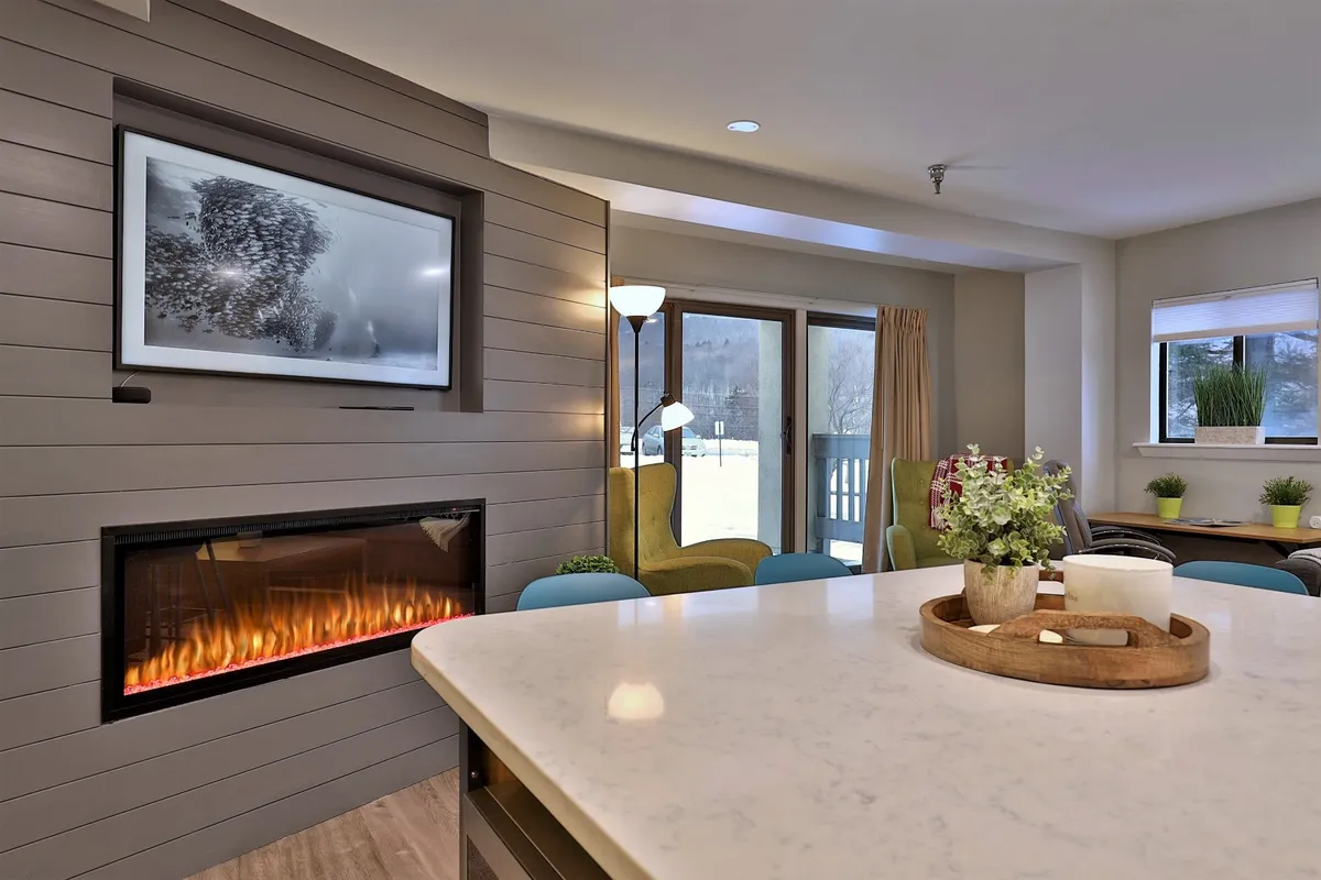 This image captures a welcoming living area featuring a fireplace, a smart television, and a dining table. The seating arrangement faces large windows (not directly visible but implied), creating a cozy environment ideal for relaxation and entertainment. The overall mood is warm and inviting, perfect for gatherings.
