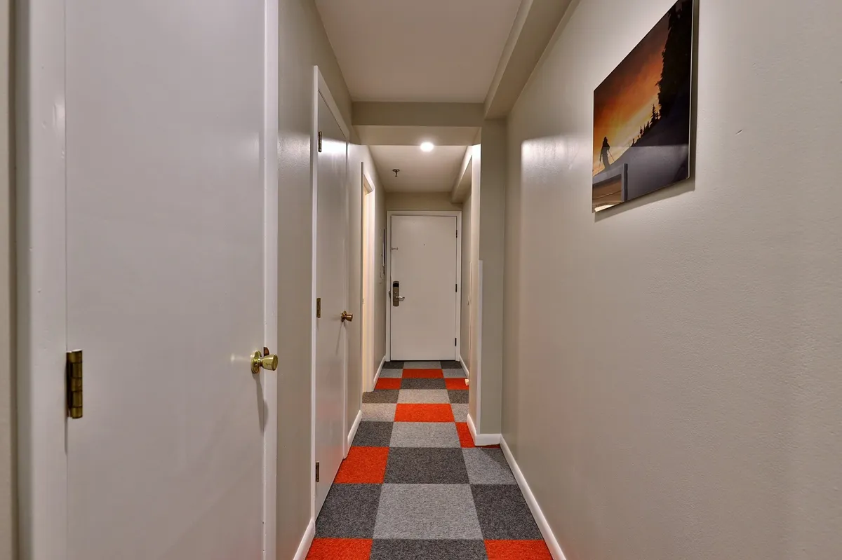 A view of a welcoming hallway, featuring a colorful carpet, open doorways, and wall art. The space is bright, inviting, and gives a sense of arrival, suggesting movement from inside to out or vice versa.